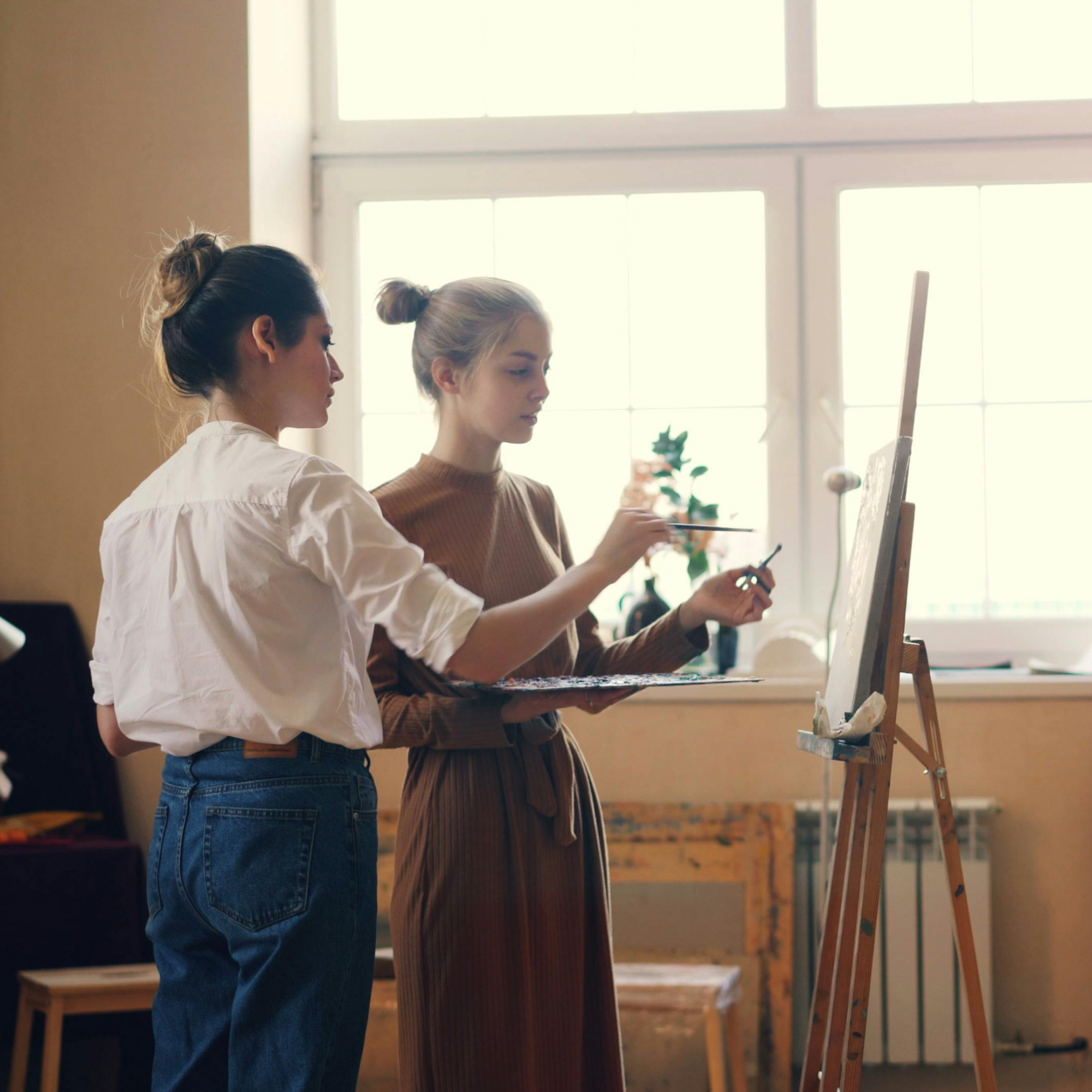 Les perfectionnements : une professeur et son étudiante sont dans une salle de classe, elles sont en train de peindre sur la même toile